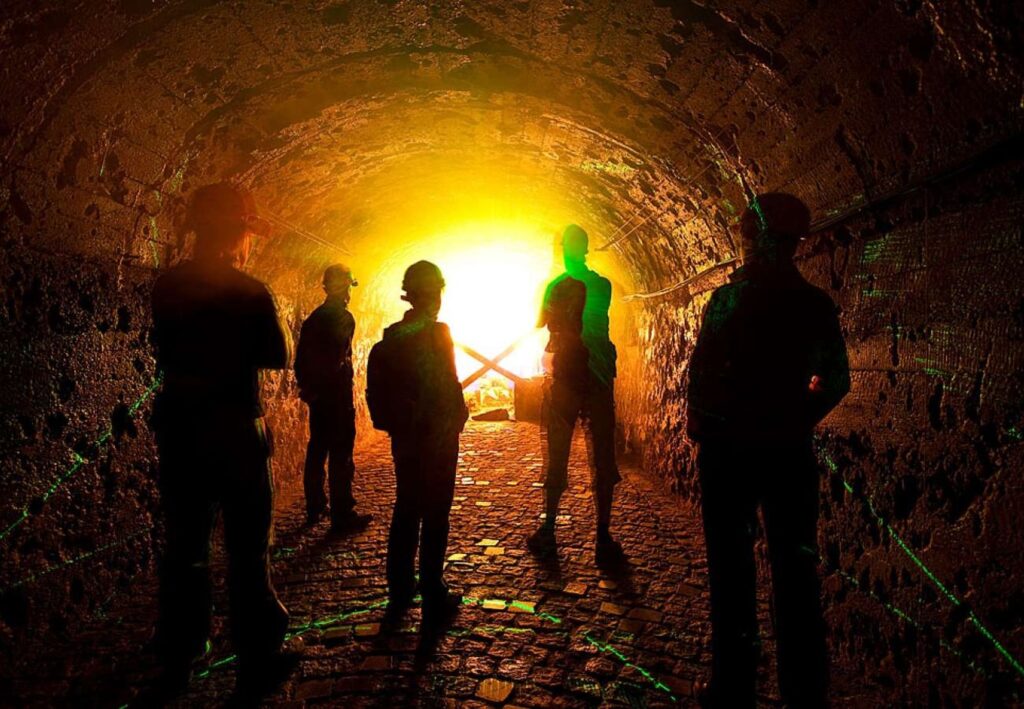 Grupa turystów w oświetlonym złotym światłem tunelu – sztolnia kopalni uranu w Kowarach, trasa zwiedzania kopalni Liczyrzepa.